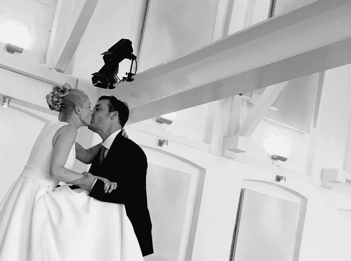 Black-and-white photo of a bride and groom kissing in Mogens Dahl Concert Hall. The romantic moment captures the couple's love in an elegant setting, perfect for a wedding celebration in a stylish concert hall.