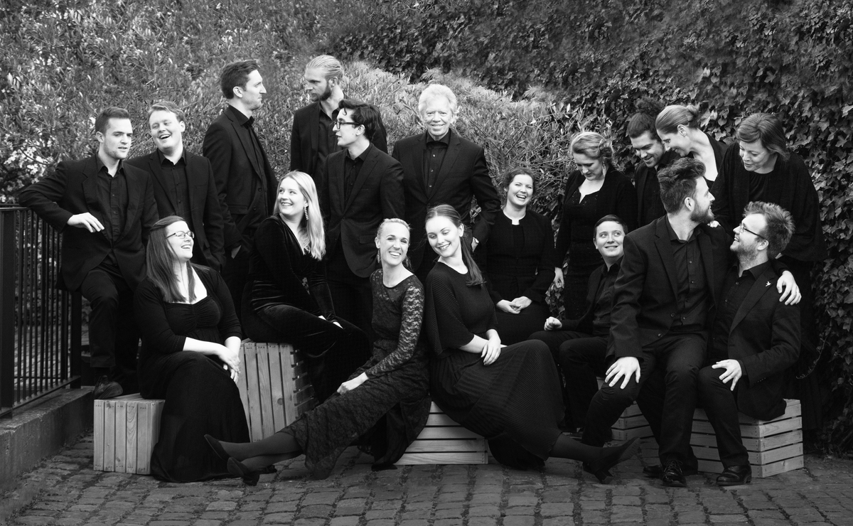 Black-and-white photo of a chamber choir standing outside Mogens Dahl Concert Hall. The choir members are gathered and posing, with an emphasis on their unity and professional appearance.