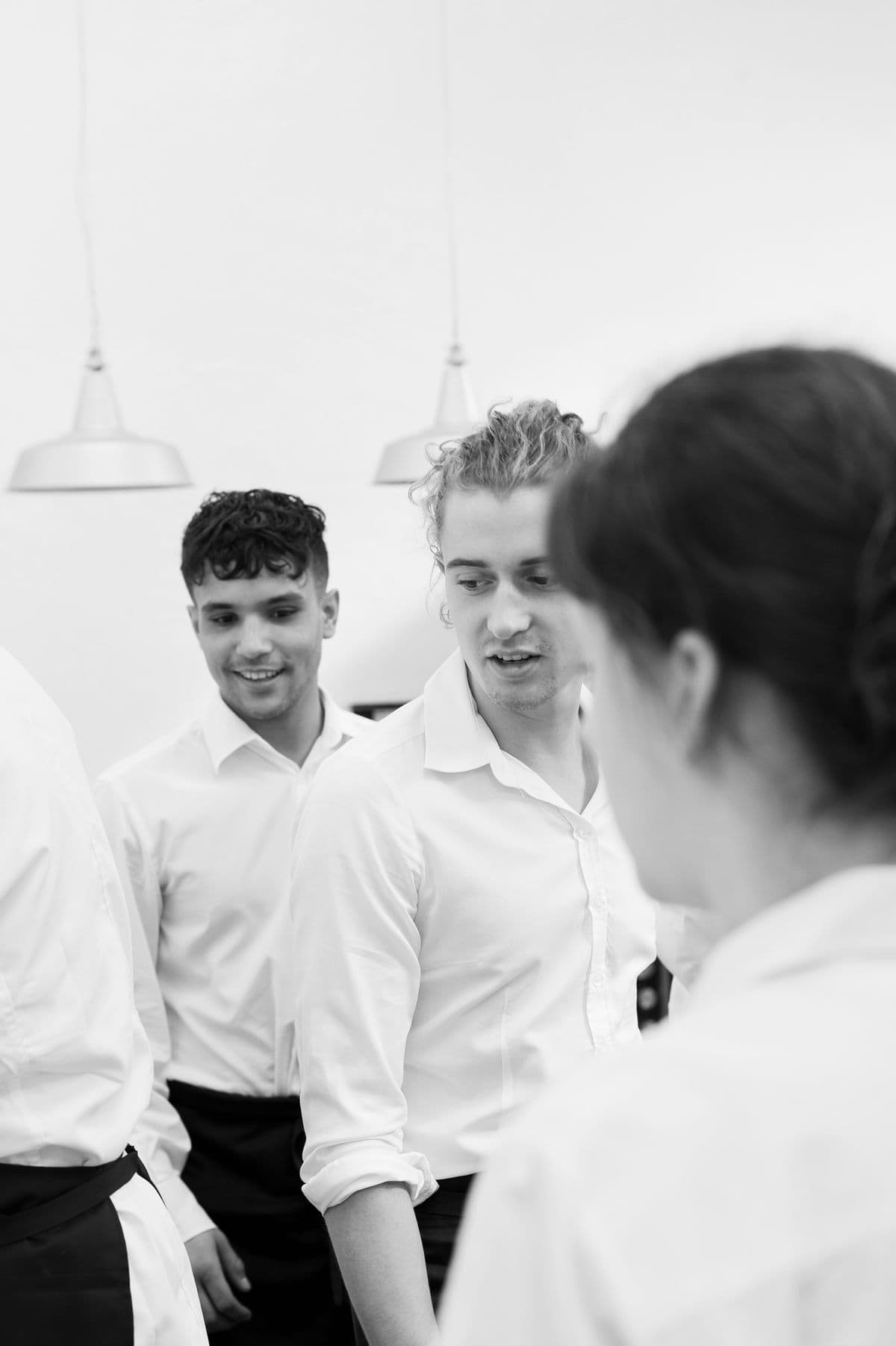 Black-and-white photo of two smiling servers at Mogens Dahl Concert Hall, captured while they are working. Focus on professional and welcoming service during events.