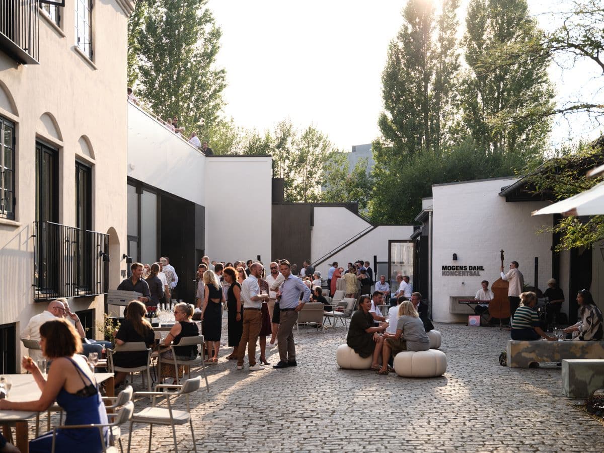 The courtyard filled with guests during an event at the Garage at Mogens Dahl Concert Hall. The picture shows the bustling and festive outdoor area where participants are enjoying the event. The lively atmosphere in the courtyard highlights the Garage's ability to create an inviting and social experience for events.