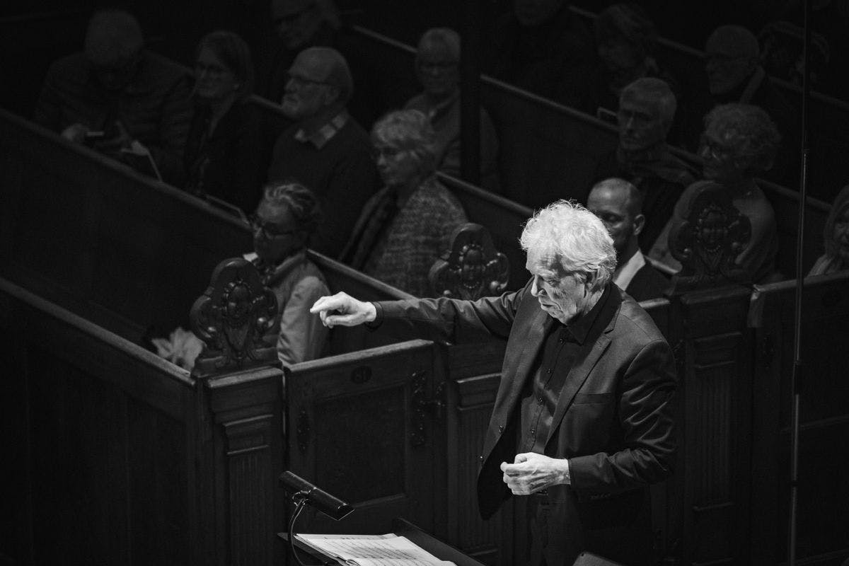 Black-and-white photo of conductor Mogens Dahl leading an orchestra during a concert at Mogens Dahl Concert Hall. The image captures his dedication and precision as a conductor, illustrating the high quality of musical experiences that have been praised in reviews of both the concert hall and Mogens Dahl Chamber Choir