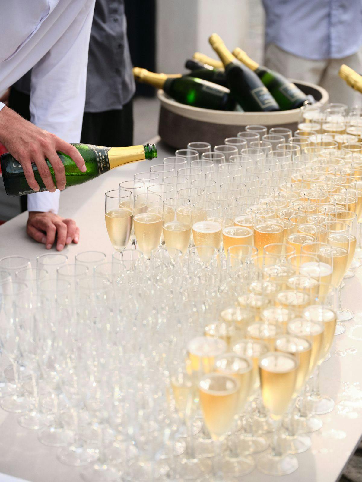 Photo of a table filled with champagne glasses at an event in Mogens Dahl Concert Hall, with a server pouring champagne into the glasses. The image showcases the festive setup and the serving of bubbles to the guests.